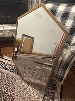 Gold metal framed vertical wall mirror with geometric shape, minor wear visible on frame and marks on mirror surface, placed on patterned carpet in front of plaid upholstered chair.