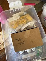 Transparent plastic box containing the label rolls and bags of yellow strings.