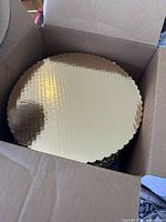 Open box showing stacked round gold scalloped cake boards.