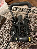 Black metal Saris trunk mount bike rack with padded upper frame support and multiple securing straps, folded and placed on a patterned rug.