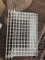 Top view of one of the three white metal wire storage baskets showing grid wire pattern and size.