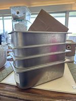 Four metal gelato pans stacked, showing their rectangular shape and stackability.