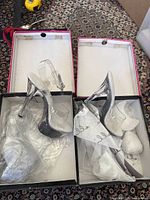Two pairs of clear high heel shoes in their original boxes with tissue paper and plastic wrapping.