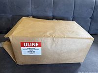 Damaged brown cardboard box labeled Uline S-14541 containing white grocery paper bags.