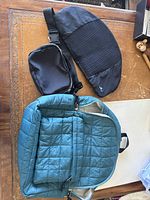 Photo showing teal padded backpack, black sling bag, and black back support pad on table.