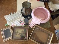 Top-down view of all items grouped together: picture frames, pink bowl, gloves, embroidered linens, metallic vase, locket, and glass comb rack.