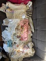 Photo showing assorted lace doilies, embroidered napkins, and crochet table runners arranged in a pile on a couch.