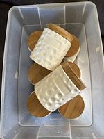 Top down image showing several white ceramic jars with bamboo lids stacked in a plastic container.