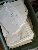 Large bin filled with stacks of flat, unfolded small white paper bakery boxes made of high-quality paper.