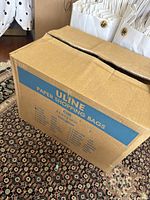 Box of Uline paper shopping bags partially opened showing white bags with twisted handles inside.
