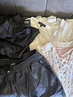 Photo showing black leather shorts by DKNY, black leather top, and multiple light-colored lace and satin tops