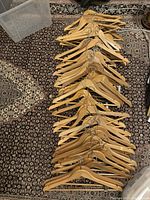 Photo showing around 40 wooden clothes hangers laid out on a rug in multiple rows. Most are standard hangers and some have pant clips attached.
