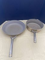 Two Calphalon pans side by side: a flat 12-inch skillet and a 3-quart saucepan with straight sides and metal handles.