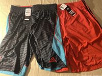 Two pairs of Adidas basketball shorts laid side by side, one black with blue and red trim, the other red with black stripes