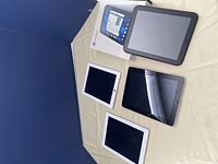 Four tablets on beige surface: three iPads (two white bezel, one black bezel) and one black HP TouchPad with retail box.