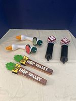 Photo showing all six beer tap handles arranged on a gray surface against a dark blue background.