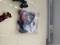 Photo showing red metal clamp, black plastic ring holder, black clamp, and sealed plastic bag with parts on a beige surface.