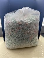 Large clear plastic bag filled with pastel colored (mainly light green and pink) foam shipping peanuts.