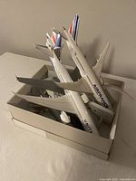 Box containing five model airplanes of various airlines including Air France and United Airlines, stacked with bases and loose parts inside a cardboard box.