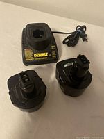 DeWALT battery charger and two rechargeable batteries shown on a flat surface with power cord partially coiled.