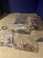 Full view of multiple costume jewelry items laid out on a beige surface in clear plastic bags including bracelets, necklaces, and earrings.