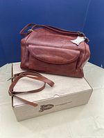 Brown leather Justin purse displayed on top of original Justin box, showing overall purse shape, front pocket and strap.