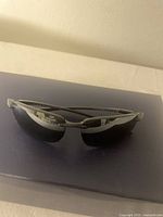 Front view of silver and black MJ Sport Hook IPA sunglasses on dark blue surface.