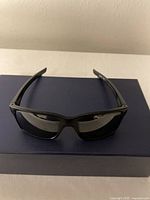 Front view of black Oakley sunglasses resting on a dark box, showing rectangular lenses and frame shape.