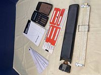Overview photo showing all items laid out including calculator, manuals, slide rule, metric converter cards, engineering scale, and circular converter fan.