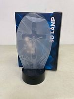 Front view of the 3D lamp showing the oval acrylic panel with engraved image of Jesus and the black base with USB port.