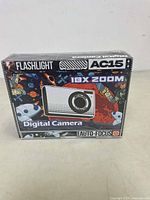 Front view of the AC15 digital camera box displaying its features such as 18X zoom, auto focus, and built-in flashlight, with colorful space-themed graphics.