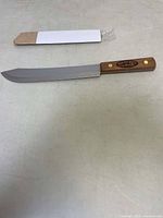 Full view of BBQ Pit Boys BBQ cutter knife next to cardboard knife sheath.