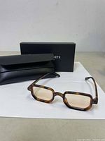 Photo of rectangular tortoiseshell glasses with black protective case and black branded box in background