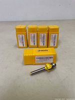 Five yellow Akylin router bit cases, one with a visible round over router bit with 1/4 inch shank and ball bearing guide removed from the case.