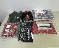 Photo showing Christmas-themed clothing, including sweaters, socks, and long sleeve items, along with wrapped gift boxes and postcards