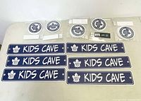 Photo showing seven circular Toronto Maple Leafs stickers and nine Kids Cave signs horizontally laid out on a surface.