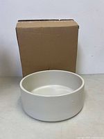 Side view of ivory ceramic potter barn pet bowl with original box in background.