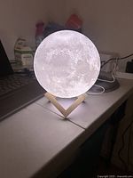 Moon lamp illuminated on wooden V-shaped base on a table next to a laptop.