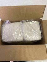 Photo showing two large sealed plastic bags of white clay inside an open cardboard box.