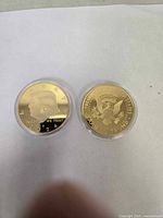 Two gold-colored tokens featuring Donald Trump's profile and presidential seal in protective capsules.