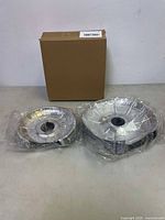 Two sizes of disposable stove burner and food drip liners wrapped in plastic, next to a brown box.