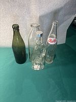 Seven vintage glass items including various bottles, a decanter, and a glass insulator displayed on green background.