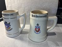 Pair of 1992 beige ceramic commemorative mugs featuring Toronto Blue Jays and York University with detailed view of front.