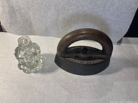 Antique iron with wooden handle and glass ink well placed side by side on a neutral background