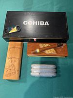 Overview of lot showing three cigar cases (Cohiba black wooden box, two light brown wooden cases), single cigar, and plastic cigar cutter