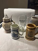 Group photo of four mugs including Avon ceramic stein, clear Montana glass mug, and two smaller ceramic mugs with ship designs