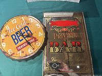 Photo showing the full clock with another wall sign behind it, highlighting the beer theme and condition of the tin clock