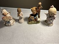 Four ceramic figurines arranged side by side on a flat surface, showing all four figurines clearly to display size and details