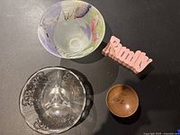 Top-down view showing the multi-colored hand-painted glass bowl, clear decorative glass bowl, small wooden bowl, and pink 'Family' sign, displayed together on black surface.