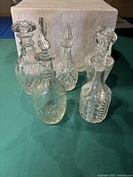 Front view of five medium-sized clear crystal decanters with varied stopper styles and cut glass patterns.